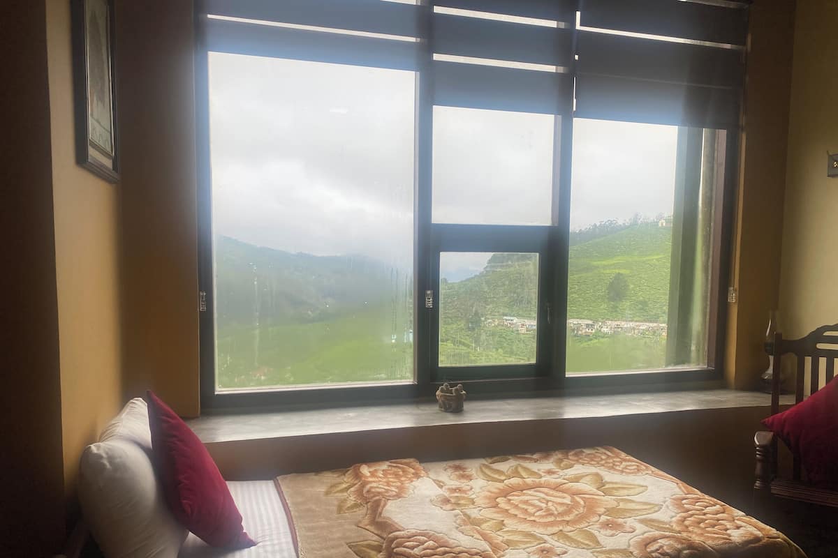Ein Schlafzimmer mit großem Fenster, einem Bett mit floraler Bettdecke und Blick auf eine grüne Landschaft.