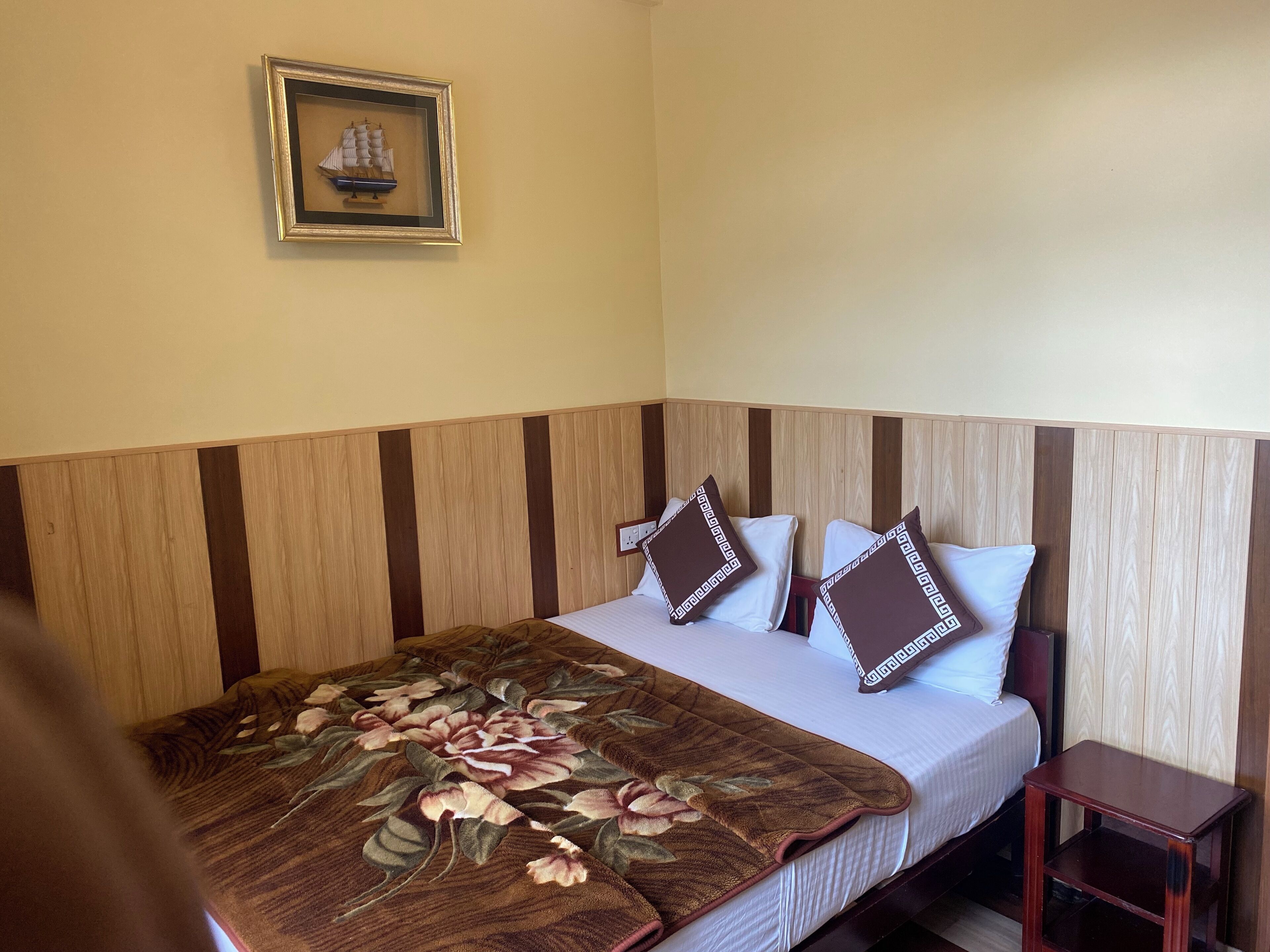 A neatly made bed with a floral bedspread, two pillows with a geometric pattern, and a small bedside table.