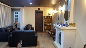 A living room with a sofa, ottoman, bookshelf, and fireplace. - House of Leisure Holiday Bungalow  (Nuwara Eliya)