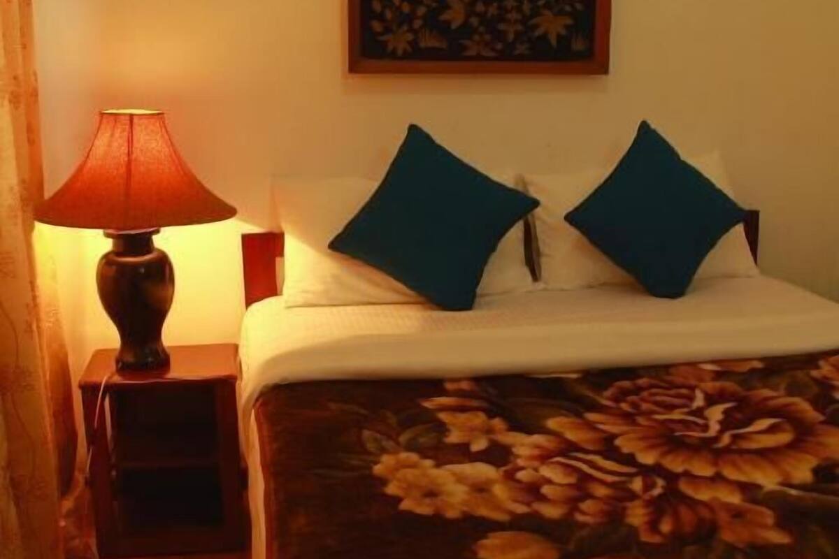 Ein Hotelzimmer mit Bett, Nachttisch und einer Lampe sowie einer zudecke mit Blumenmuster.