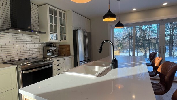 Een moderne keuken met een centraal eiland, roestvrijstalen apparatuur en hangende lampen.