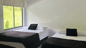 A room with two beds, a window with a view of greenery, and a wooden ceiling.