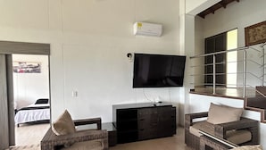 A spacious living area with a large flat-screen TV mounted on the wall, a comfortable sofa set, and a wooden ceiling.