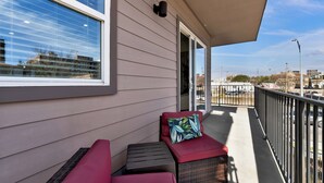 A balcony with a red cushioned seating area, a small table, and a view of the cityscape. - NEW Modern 1BR in Oak Lawn Dallas With Free Parking + Complimentary EV Charger (Dallas)