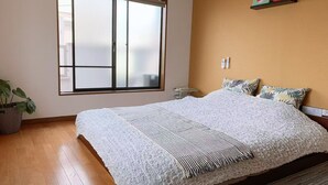 A bedroom with a large bed, a window, a bedside table, a plant, and a wall-mounted shelf with two decorative items. - Guest house Chiharu" 6 rooms, 12 people MAX ・ 4 minutes from JR Teradacho station, near Tennoji USJ direct access hot spring (ikunonishi, ikuno ward, Osaka city)