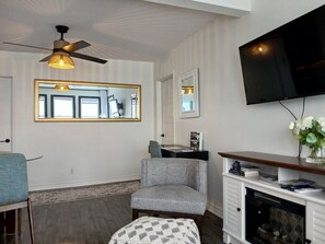 A living room with a ceiling fan, a TV, a fireplace, a large mirror, and a seating area.