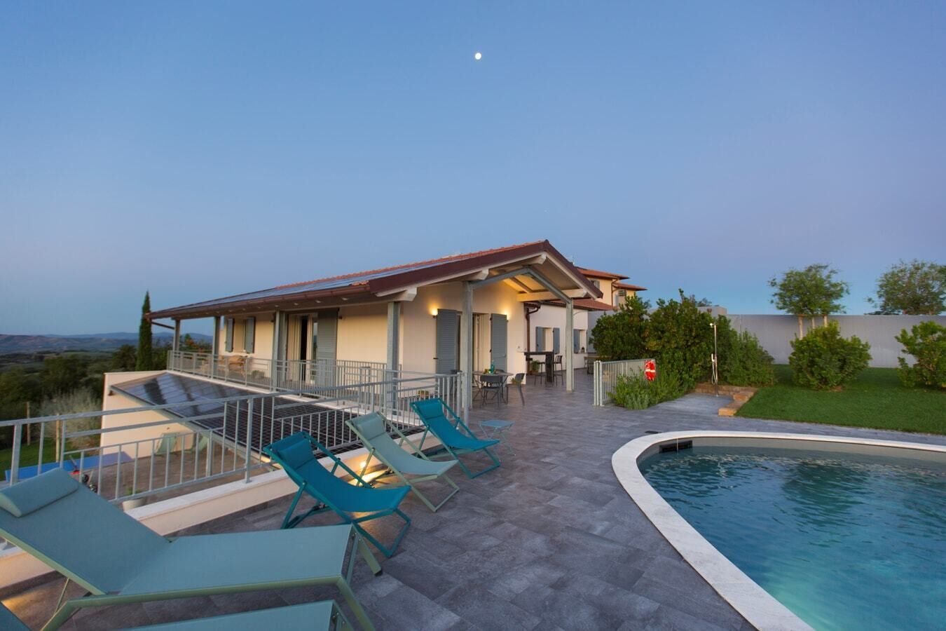 A poolside area with lounge chairs, a covered patio, and a view of the landscape.