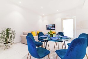 Ein moderner Essbereich mit einem runden Tisch, blauen Stühlen und einem Fernseher an der Wand.