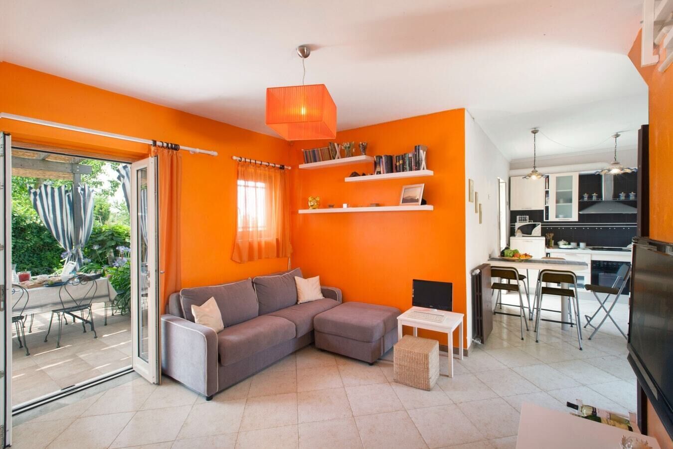 Un saló modern amb un sofà seccional gris, una taula blanca petita, i una zona de cuina amb una taula de dinar i cadires.