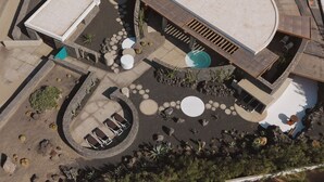 Luchtbeeld van een modern gebouw met een rond zwembad, buitenmeubilair en diverse planten.