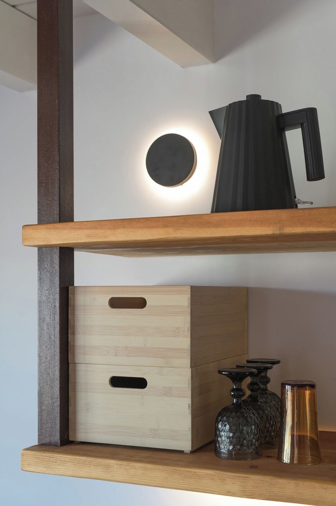 Uno scaffale in legno con una lampada sferica, un oggetto nero e due contenitori di vetro.