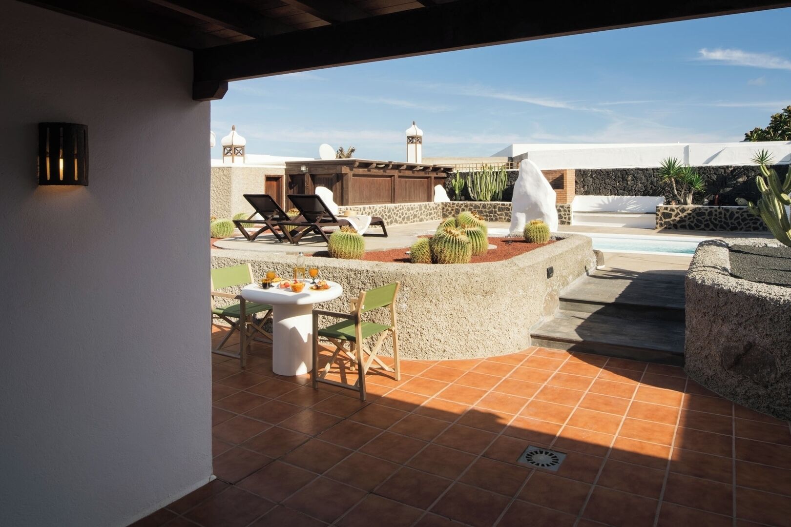 Un patio con mesa y sillas, una piscina y cactus.