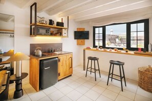 A compact kitchen with a refrigerator, a microwave, and a sink. There are two stools and a window with a view of the city. - Canaryislandshost I Esencia II (Urbanización Famara)
