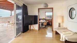 A modern living room with a TV, a sofa, and a dining area with chairs and a table. - Canaryislandshost I Esencia (Urbanización Famara)