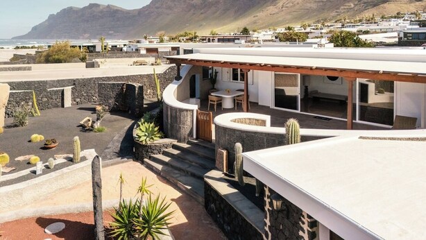 A modern building with a flat roof, outdoor seating area, and a view of the sea and mountains. - Canaryislandshost I Esencia (Urbanización Famara)