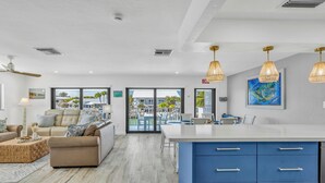 A modern living room with a large sofa, a coffee table, and a dining area with a white table and blue cabinets. - Waterfront Escape, Private Dock, Cabana Club, Keys Paradise (Key Colony Beach)