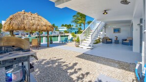 A beachside patio with a thatched umbrella, outdoor seating, a pool, and a staircase leading to a covered area. - Waterfront Escape, Private Dock, Cabana Club, Keys Paradise (Key Colony Beach)