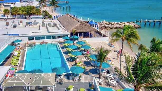 A resort with a large swimming pool, beach umbrellas, lounge chairs, and a pier extending into the ocean. - Waterfront Escape, Private Dock, Cabana Club, Keys Paradise (Key Colony Beach)