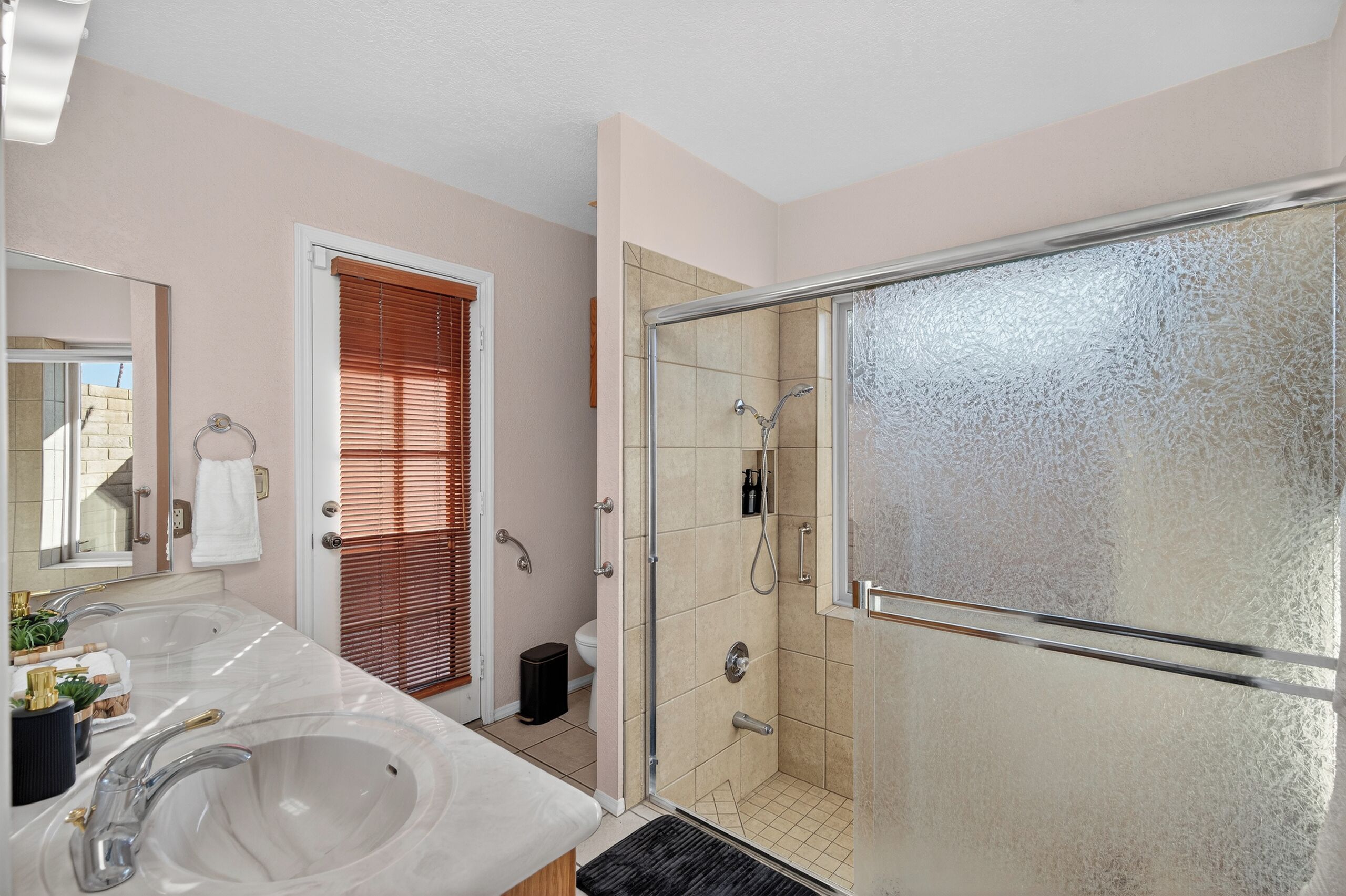 A bathroom with two sinks, a shower, and a glass door.