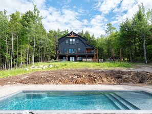 Ein modernes, zweistöckiges Haus mit Balkon, umgeben von Wald und einem Schwimmbad.
