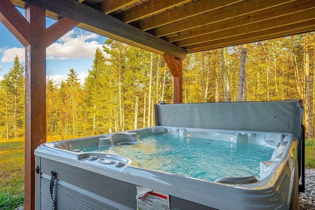 A hot tub under a wooden pergola with a forest backdrop.