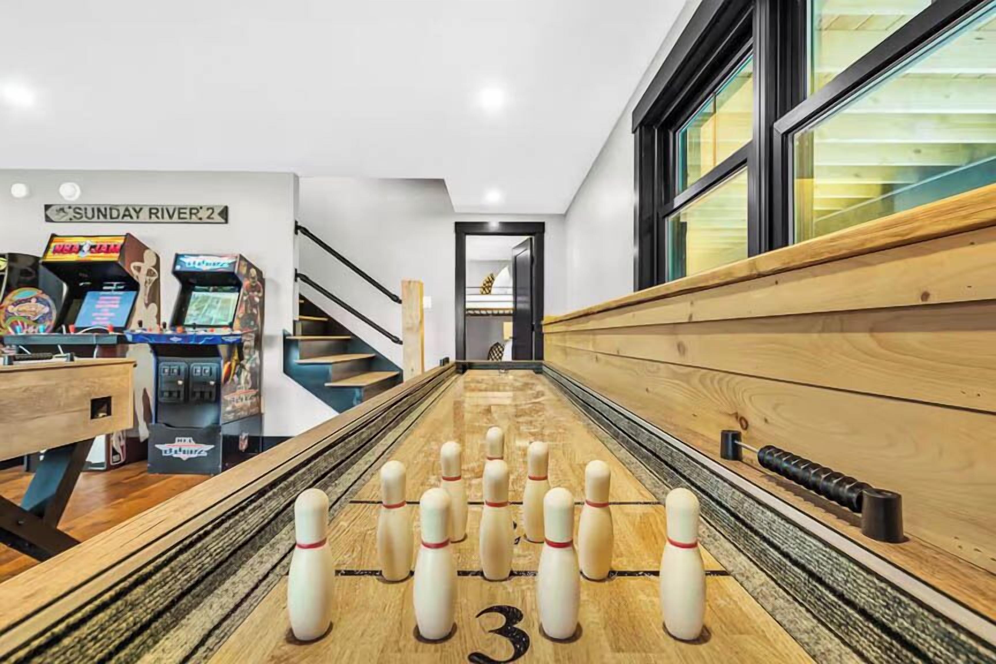 A bowling alley with a wooden floor, numbered pins, and a sign reading "SUNDAY RIVER 2".