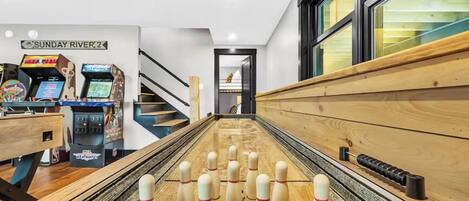 A bowling alley with a wooden floor, numbered pins, and a sign reading "SUNDAY RIVER 2".