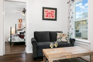 A living room with a black sofa, a wooden coffee table with two wine glasses, and a framed artwork above the sofa. - Windmill Haus | 2/2, Hot Tub (Fredericksburg)