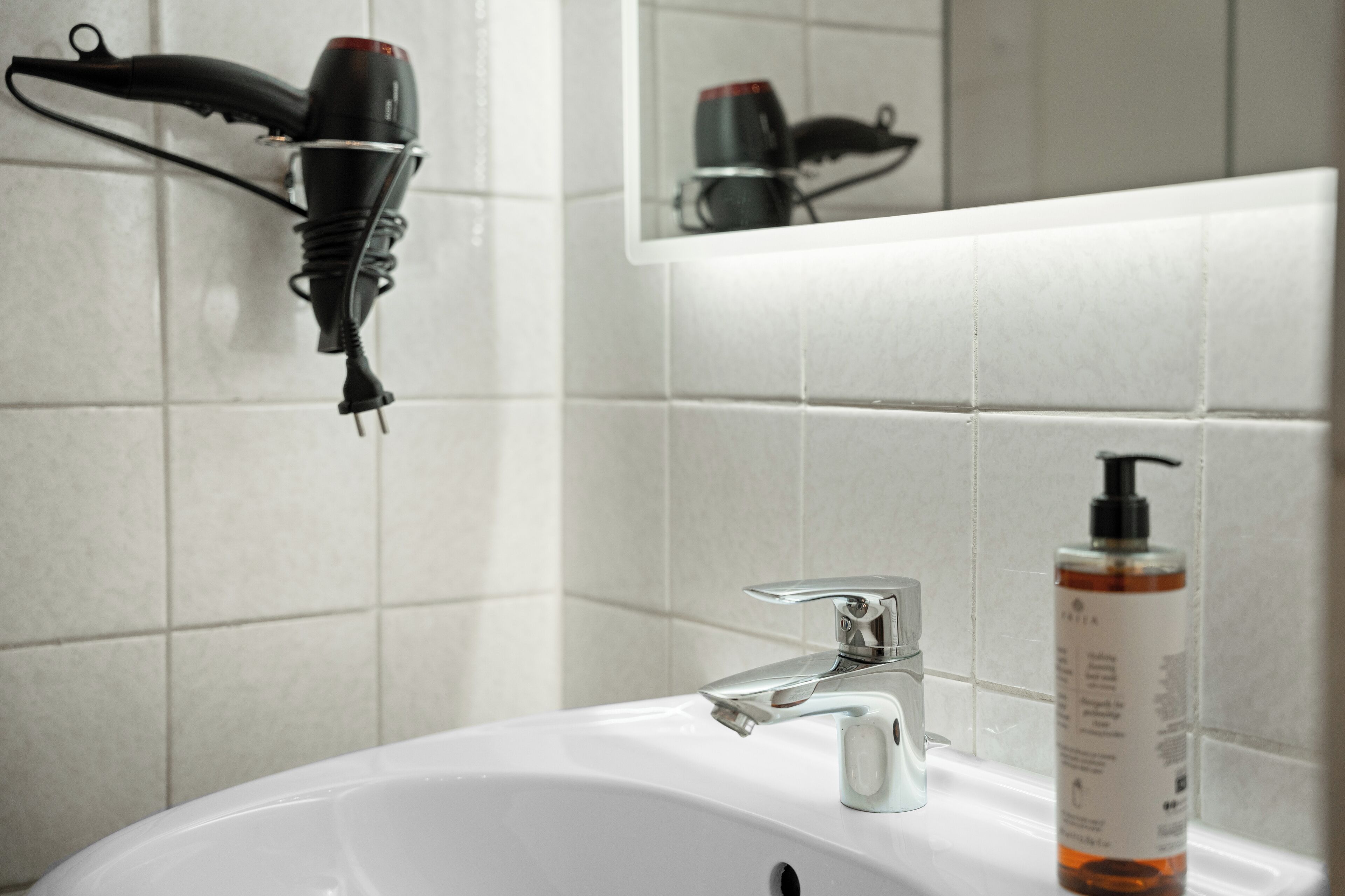 Ein Badezimmer mit Waschbecken, Spiegel und einem an der Wand montierten Föhn.