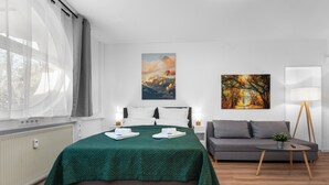 A modern hotel room with a large bed, a grey sofa, a small table with a plant, and two paintings on the walls. - Central | Kitchen | WLAN | 58 sqm (Solingen)