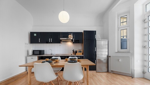 A modern kitchen with black cabinets, a wooden dining table, and white chairs. - Central | Kitchen | WLAN | 58 sqm (Solingen)