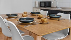 A dining table set with plates, bowls, and cups, surrounded by white chairs in a modern kitchen with a microwave and cabinets. - Central | Kitchen | WLAN | 58 sqm (Solingen)