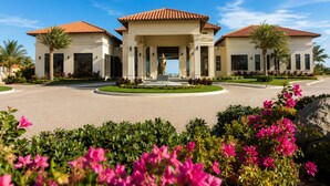 A two-story building with a central entrance, surrounded by a landscaped garden with pink flowers and palm trees. - Gold Coast Aruba  (Noord)