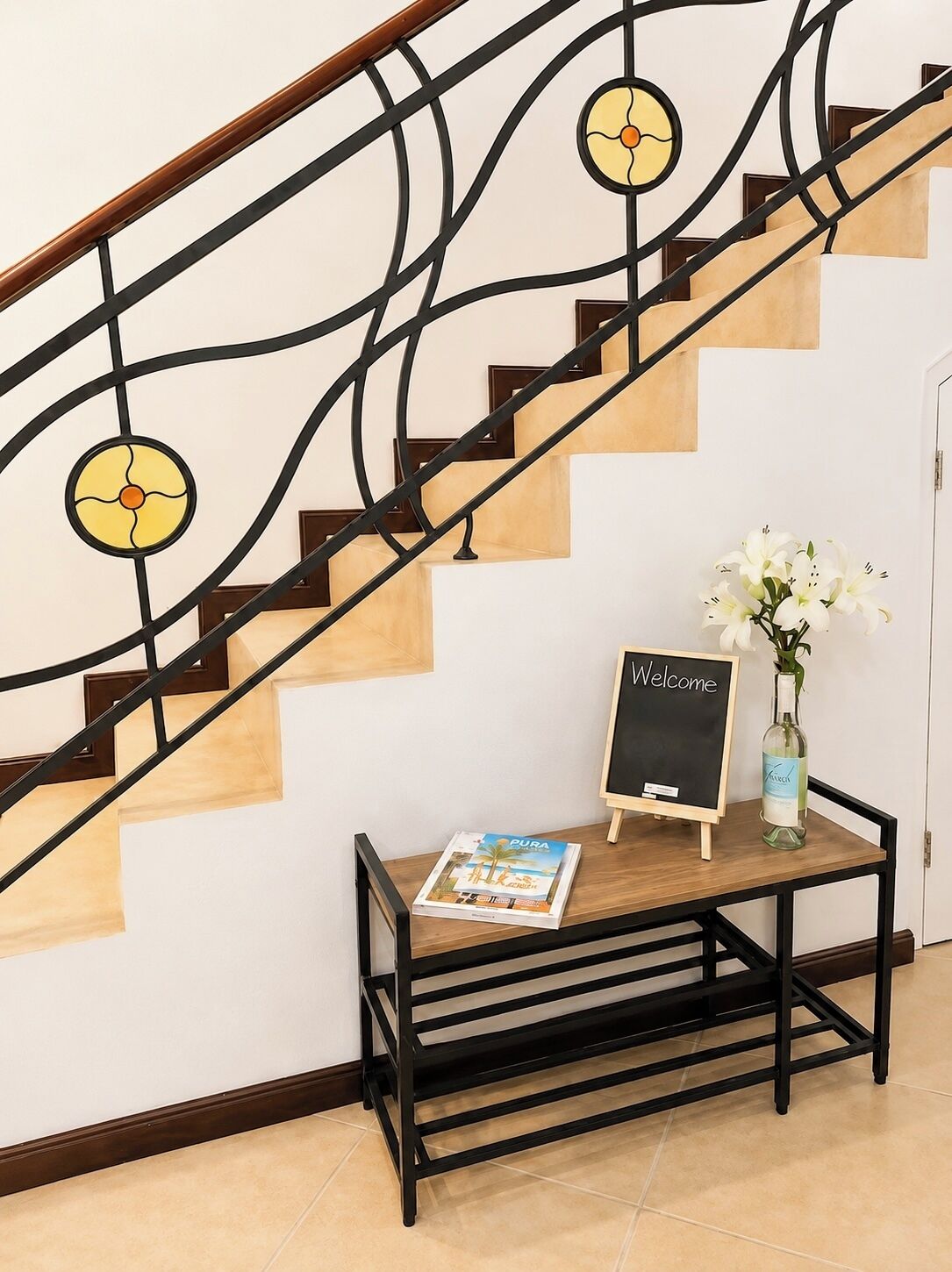 Un escalier orné d’une rampe décorative, une pancarte de bienvenue, un magazine et un vase rempli de fleurs.