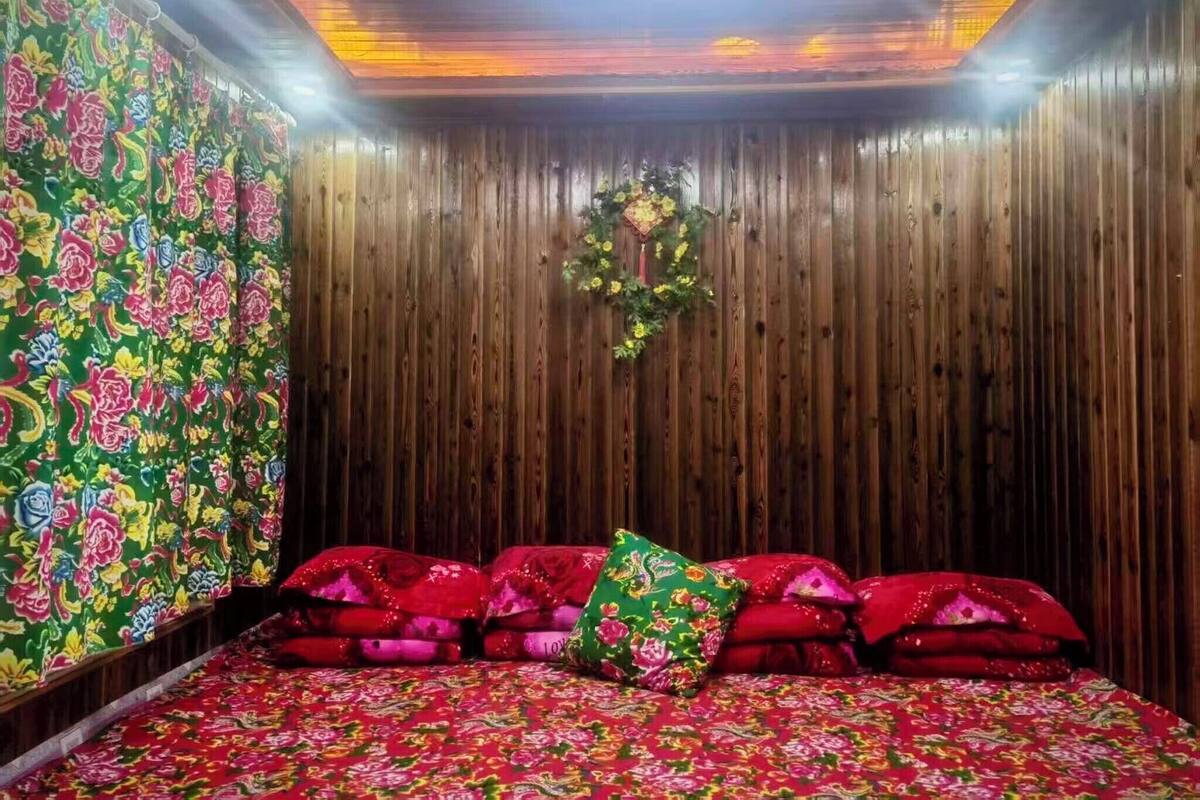 A room with a wooden wall, a floral-patterned bedspread, and a decorative wreath on the wall.
