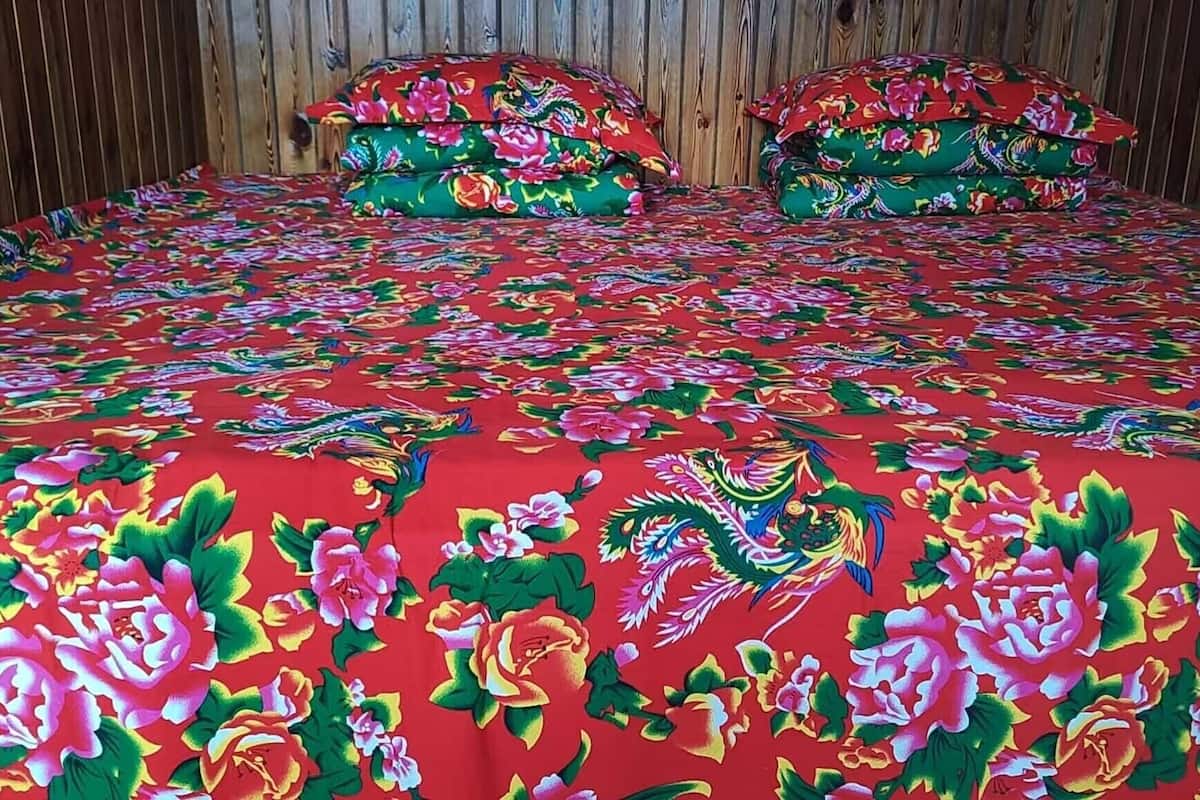 A bed with a red floral bedspread and matching pillows, set against a wooden wall.
