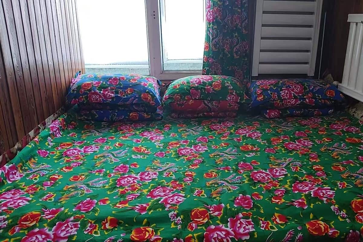 A room with a green floral bedspread, wooden walls, a window with curtains, and a white radiator.