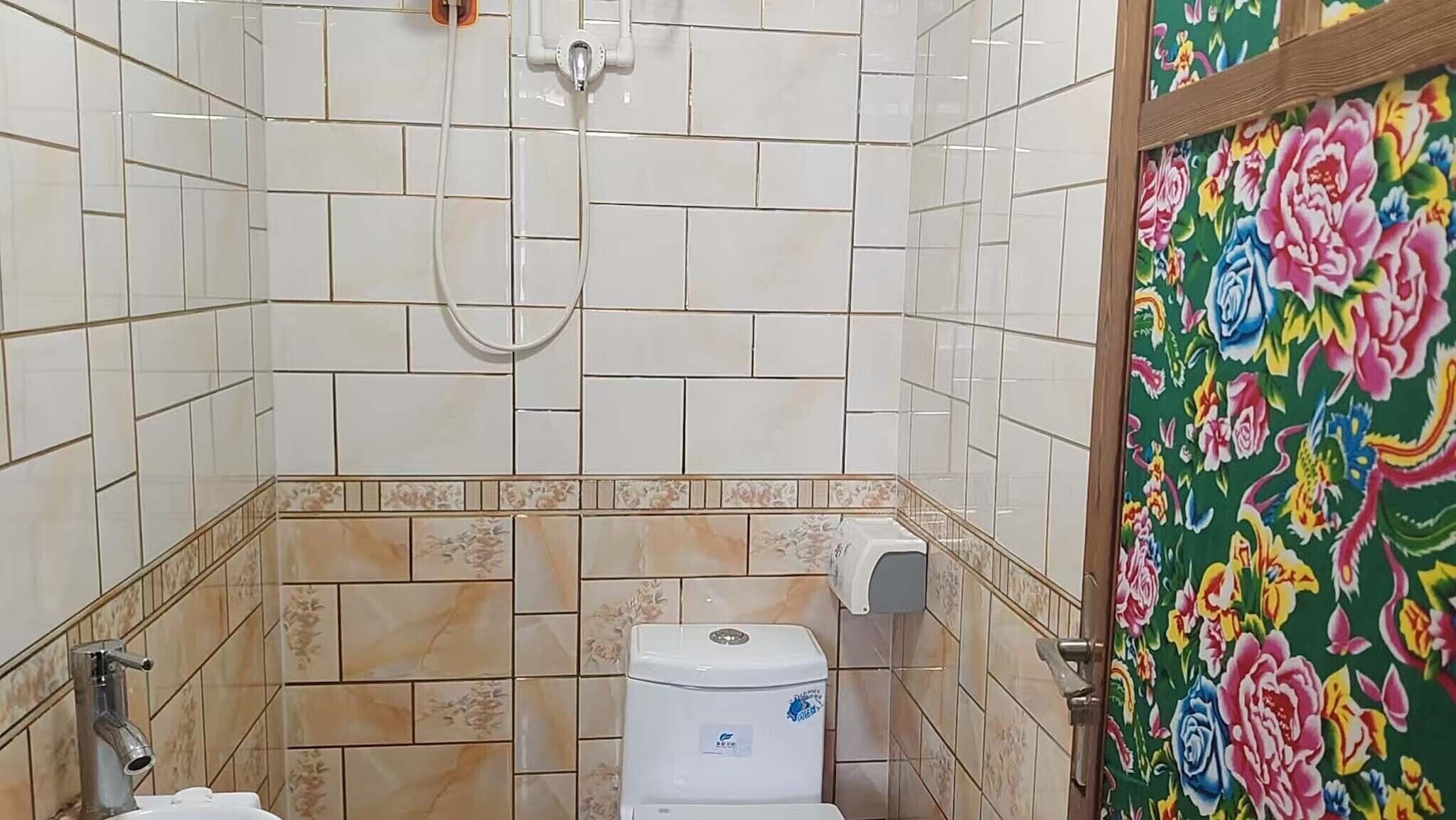 A bathroom with white tiles, a toilet, a shower, and a door with a floral pattern.