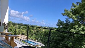 Een balkon met een zwembad, buitenmeubilair en uitzicht op weelderige begroeiing.