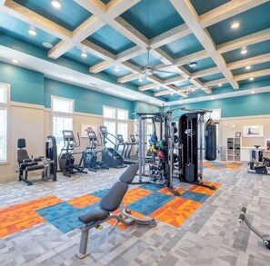 Ein Fitnessraum mit Trainingsgeräten, einem Deckenventilator und einem gemusterten Boden.