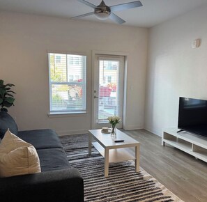 Ein Wohnzimmer mit einer Couch, einem Couchtisch, einem Fernseher und einem Deckenventilator.
