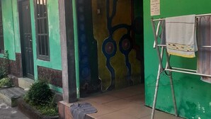 A building with green walls and a colorful mural. There is a clothes drying rack with a towel hanging on it. - Nyaman Homestay (Pare)