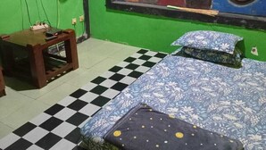 A room with a checkered floor, a bed with floral bedding, a green wall, and a painting. - Nyaman Homestay (Pare)
