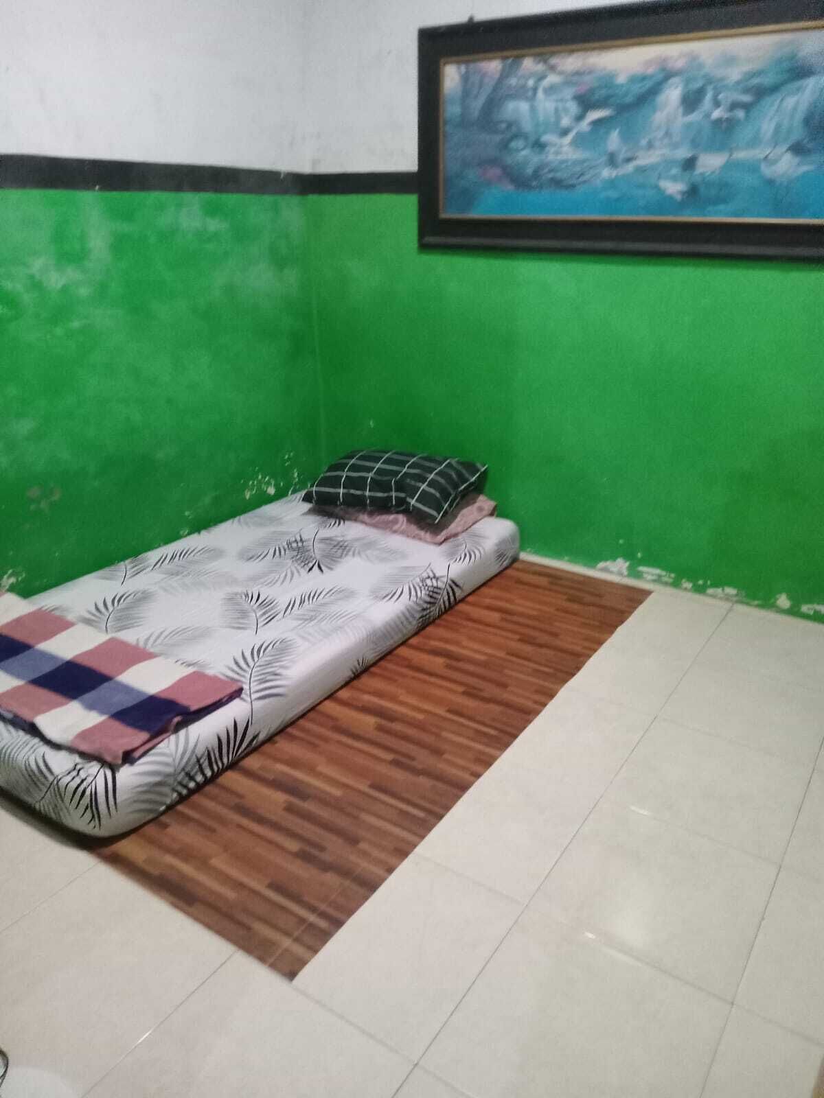Una habitación pequeña con cama, paredes verdes, un cuadro enmarcado y piso de madera.