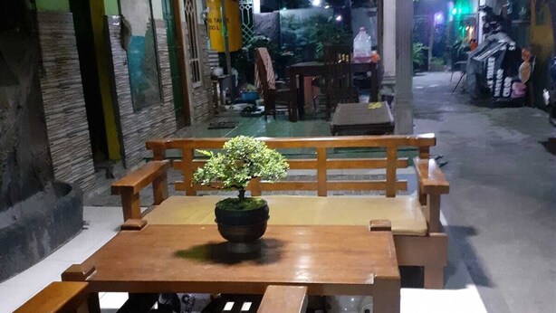 An outdoor dining area with a wooden table and benches, a potted plant on the table, and a tiled floor. - Nyaman Homestay (Pare)