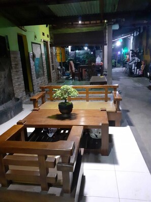An outdoor dining area with a wooden table and benches, a potted plant on the table, and a tiled floor. - Nyaman Homestay (Pare)