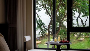 A bedroom with a large window, a bedside table with candles, and a view of trees and greenery outside. - Lijiang Ancient City Hitone Resort (Lijiang)
