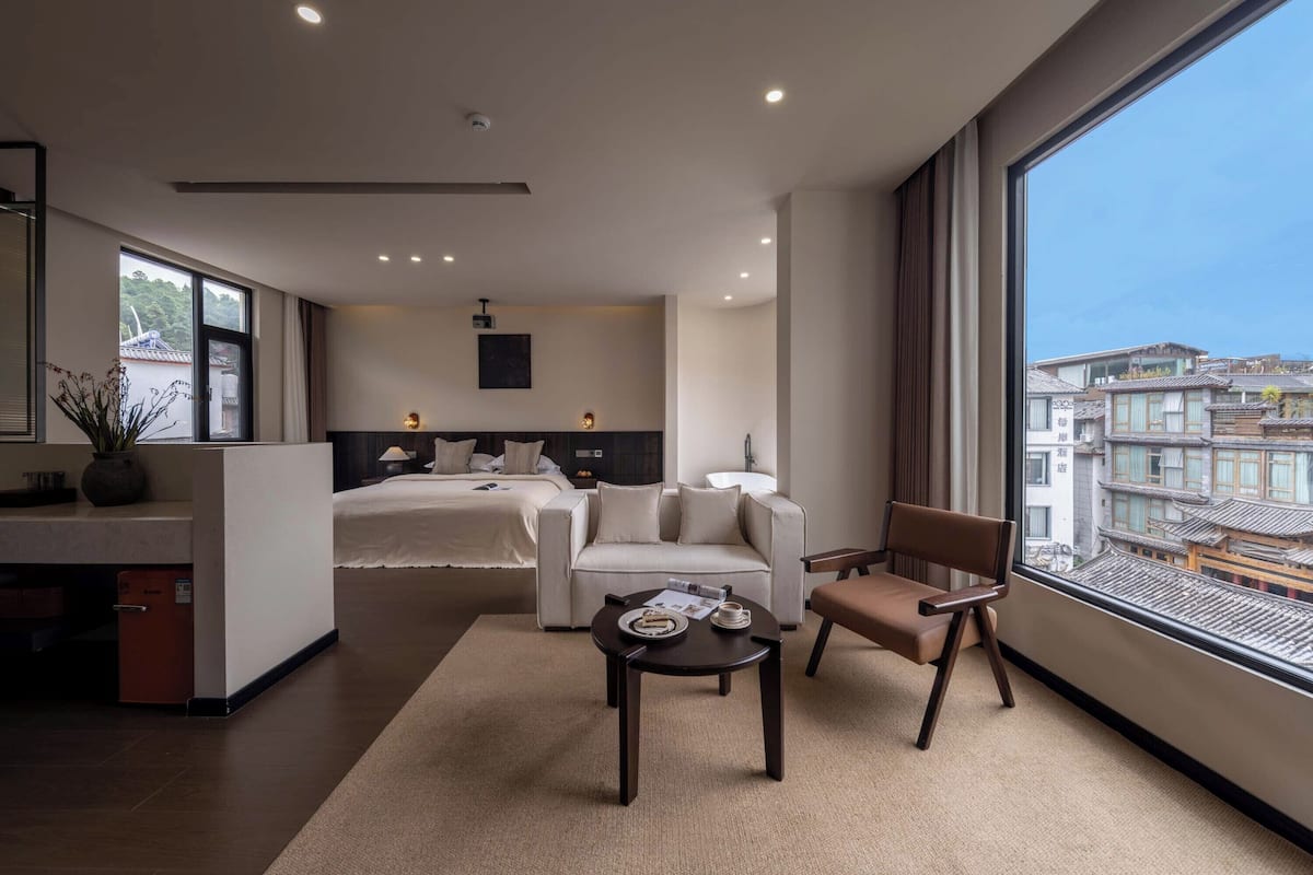 Ein modernes Hotelzimmer mit einem großen Bett, einer Sitzecke, einem kleinen Tisch und Blick auf traditionelle Gebäude.