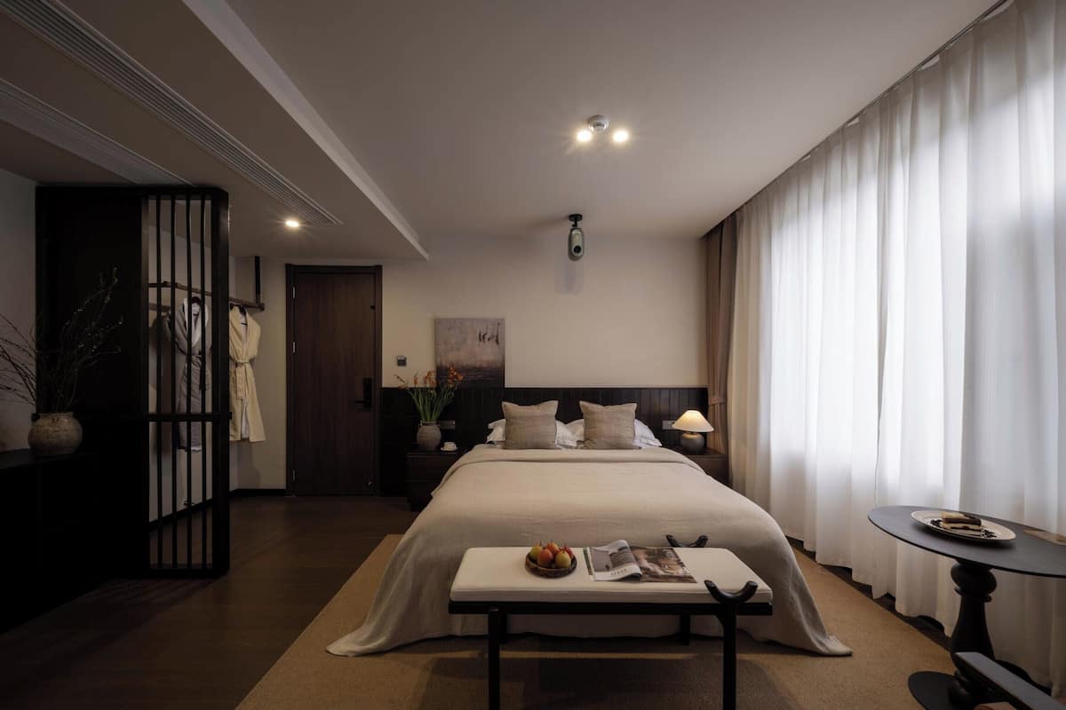 Ein modernes Hotelzimmer mit einem großen Bett, einem Nachttisch und einem kleinen runden Tisch mit einer Teller voller Speisen.
