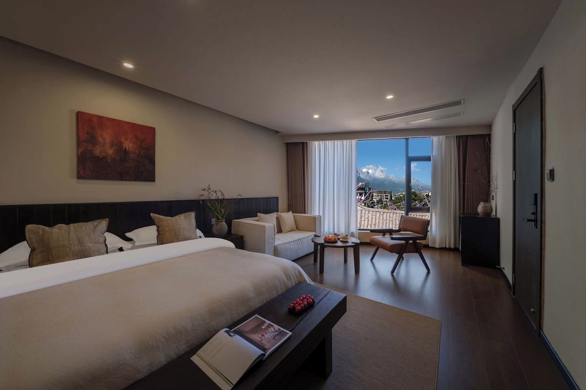Ein modernes Hotelzimmer mit einem großen Bett, einer Couch, einem kleinen Tisch und Bergblick.